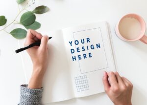 Company logos signified by an artist's hand on top of a notebook on a table