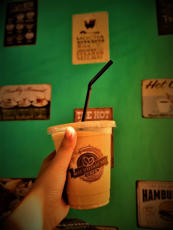 someone holding an 8oz-size Iced coffee on a green wall background