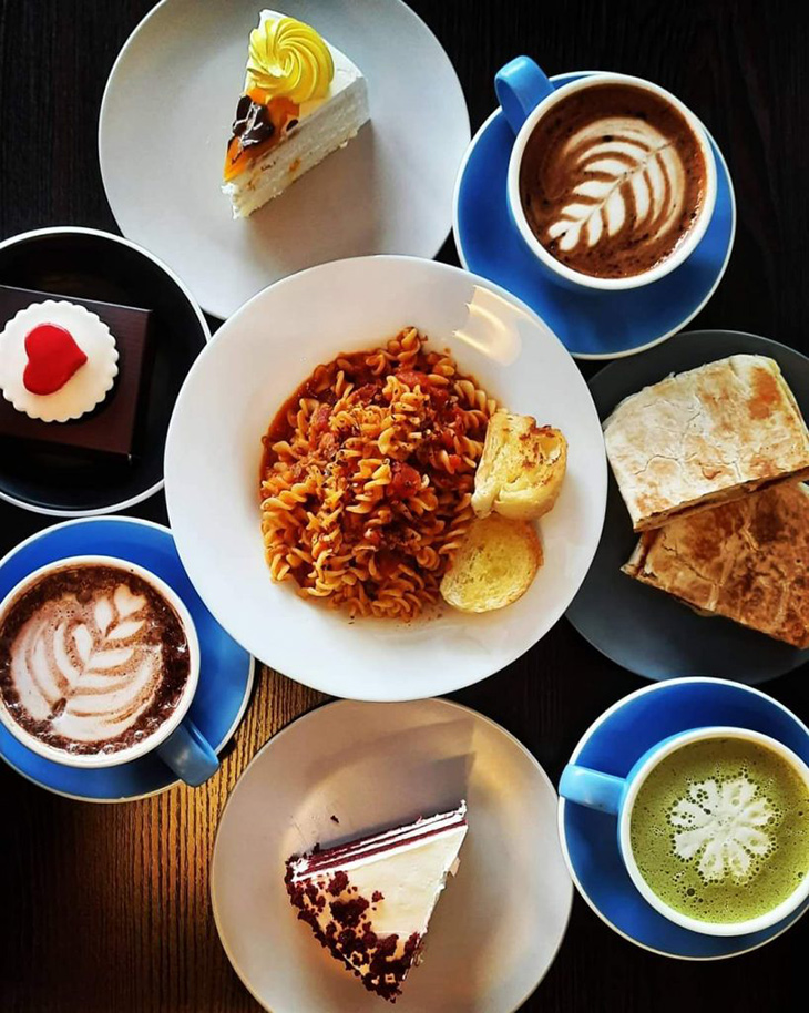 Flat lay of food and drinks. Pasta in the center with three drinks and slices of cakes on its side