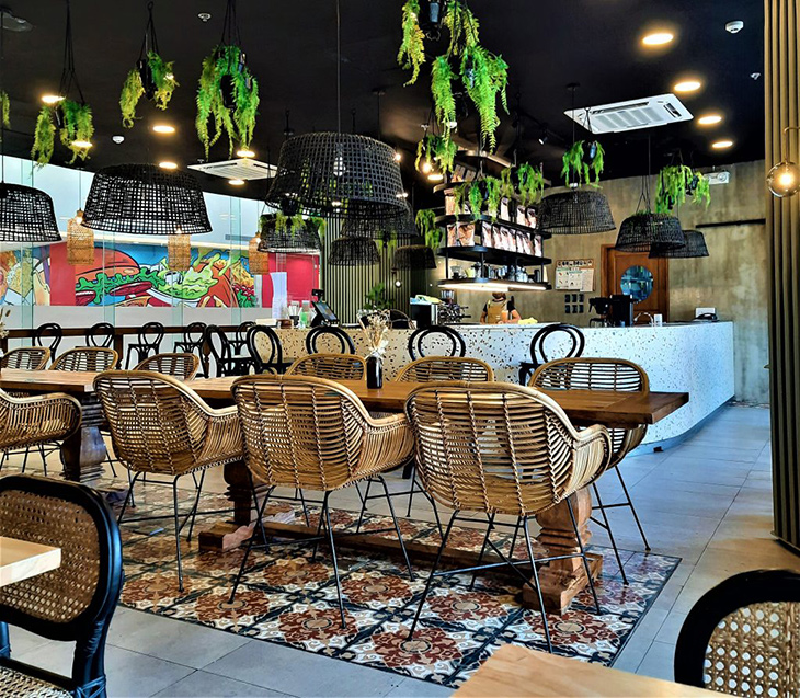 Coffee shop with chairs and pendant lighting made of rattan, wooden tables, and hanging plants