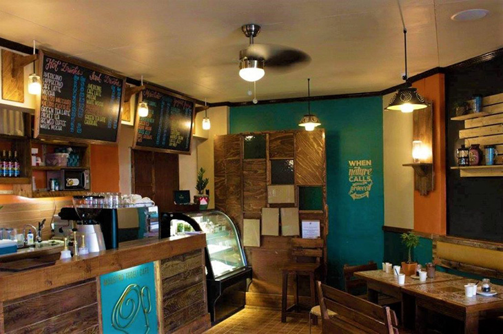 A coffee shop with coffee counter with menu, light pendants, and wooden tables and chairs