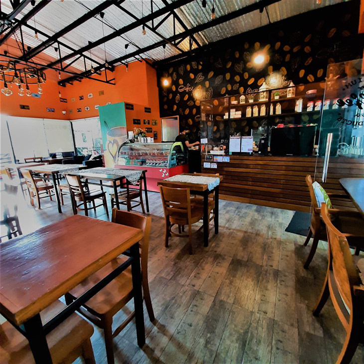A coffee shop with wooden chairs and tables, orange walls, and coffee bean wallpaper on the coffee counter