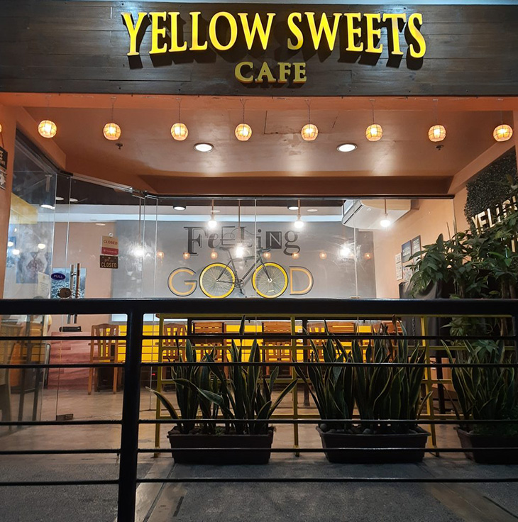 Storefront of a café with plants, light pendants, and wall paint of Feeling Good