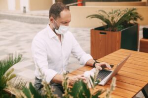 an adult male businessman in a mask sits on the street in a cafe communicates on with his virtual assistant