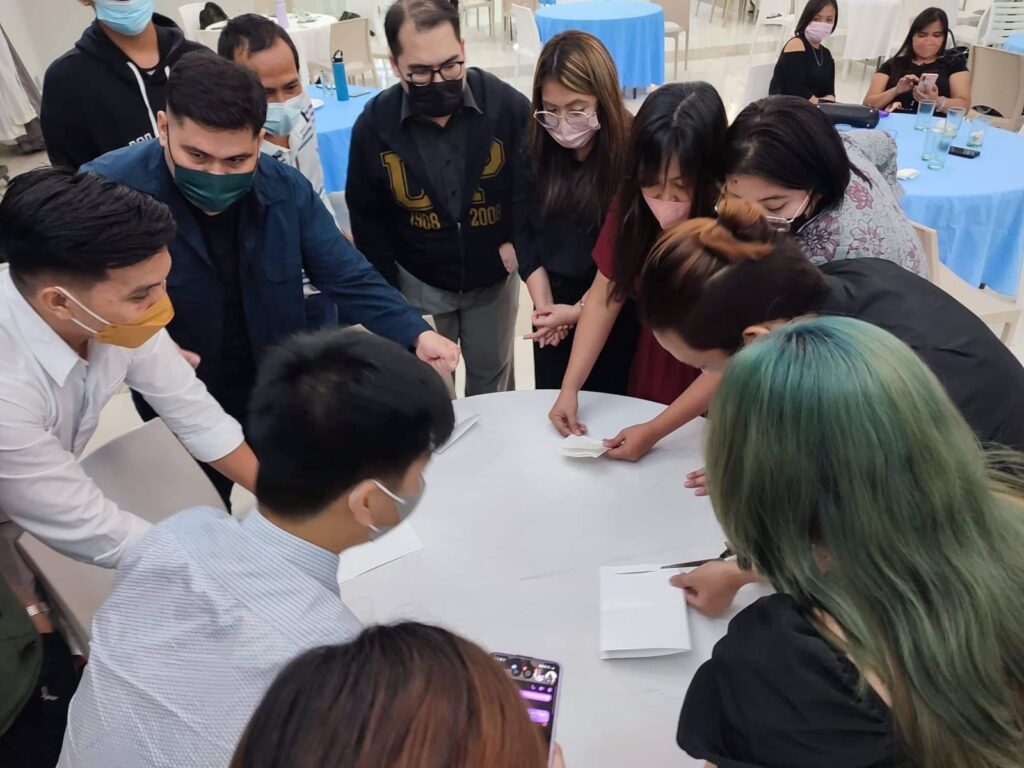 Team members of group 1 strategically plan on how to cut and make a big circle using one bond paper.