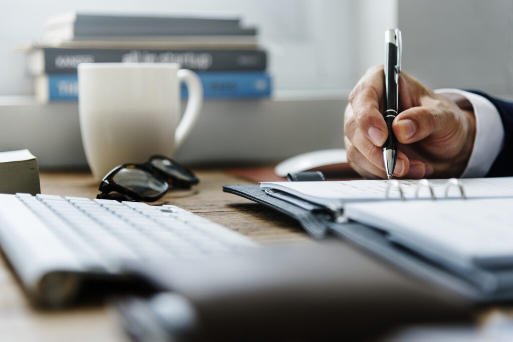 An office table featuring a man’s hand while writing notes