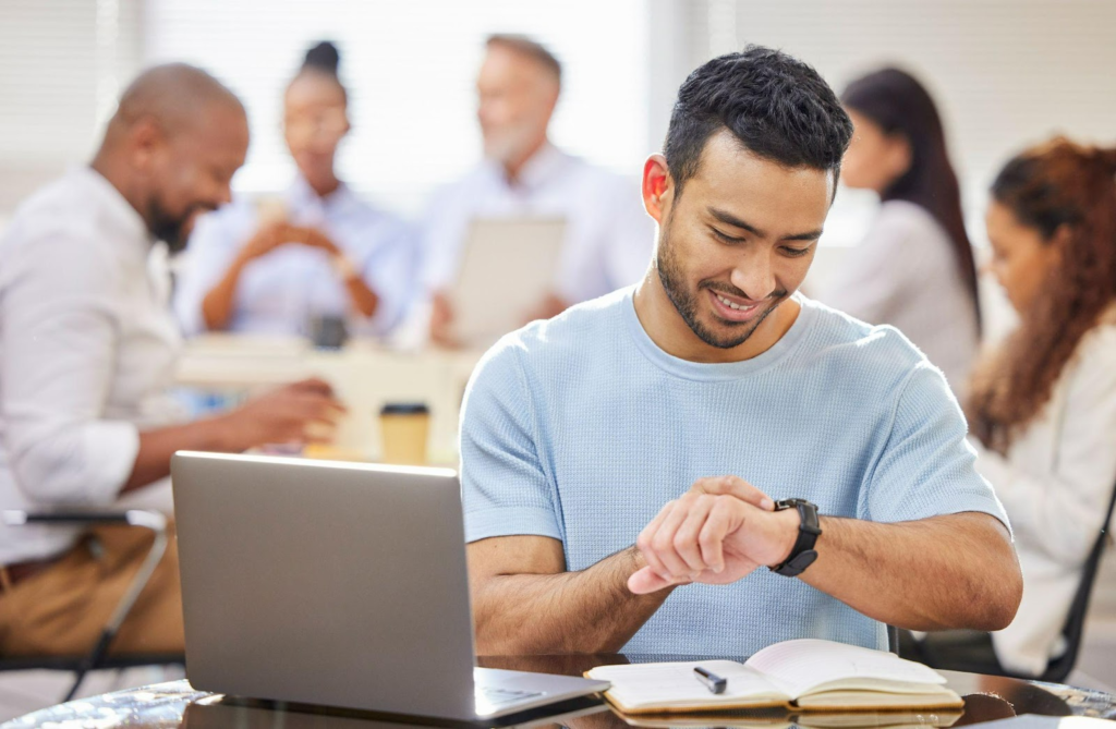 man looking at his watch while working on his laptop